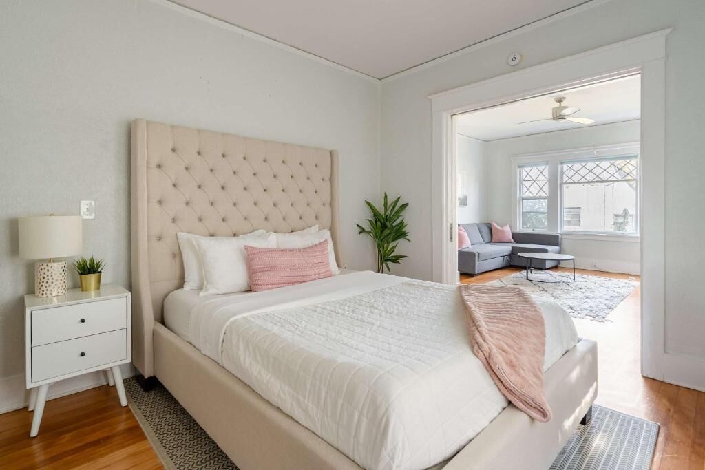 A bedroom with a bed, bedside table, lamp, and a view of another room.