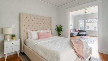 A bedroom with a bed, bedside table, lamp, and a view of another room.