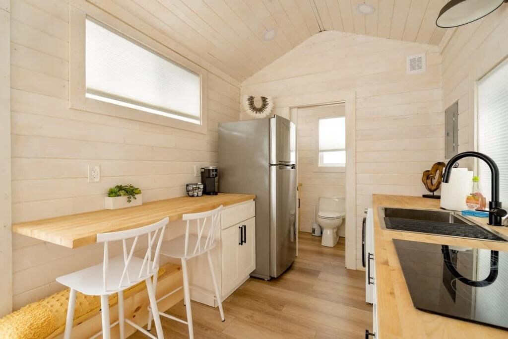 A compact kitchen with a wooden countertop, white chairs, a stainless steel refrigerator, and a black range hood.