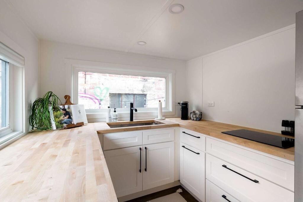 A modern kitchen with white cabinets, a wooden countertop, a sink, and a window.