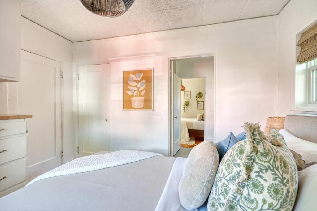 Ein Schlafzimmer mit Bett, Tür, Wandpflanze und Fenster.