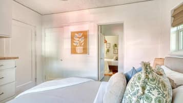 Un dormitorio con cama, puerta, planta en la pared y ventana.