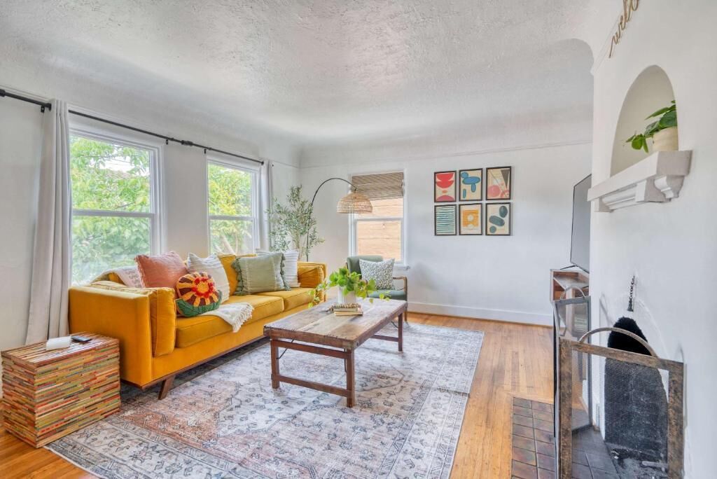 A living room with a yellow sofa, a coffee table, and a fireplace.