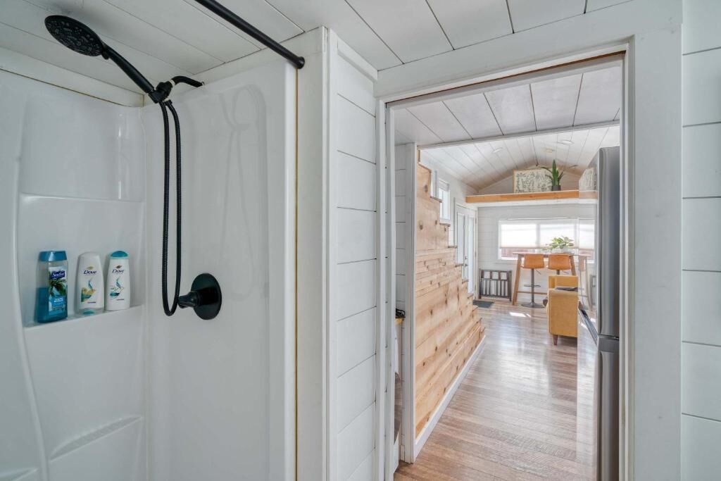 Un pasillo que conduce a una cocina con paredes de madera y una puerta blanca con cabezal de ducha y artículos de aseo.