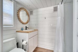 A compact bathroom with a wooden vanity, a round mirror, a toilet, and a shower curtain.