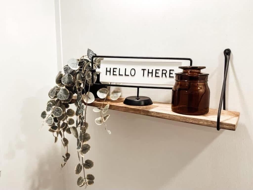 Una estantería con un cartel que dice 'HELLO THERE', un frasco marrón y plantas colgantes.