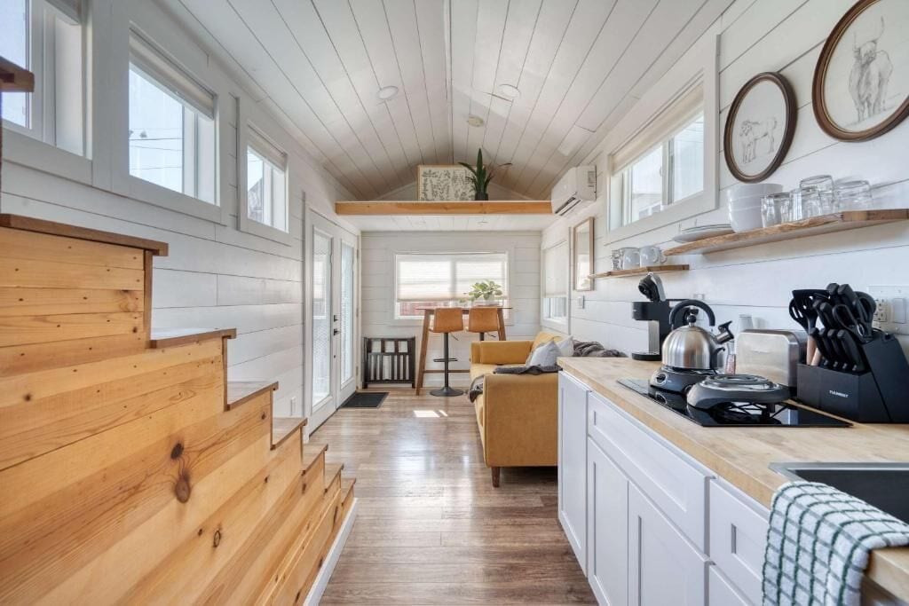 Een moderne keuken met houten kastjes, een eethoek met een tafel en stoelen, en uitzicht op het landschap door grote ramen.