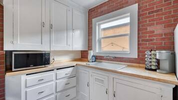 Una cocina con armarios blancos, microondas, pileta y cafetera.