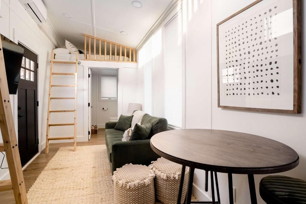 A modern room with a bunk bed, a round table, a sofa, and a framed artwork on the wall.