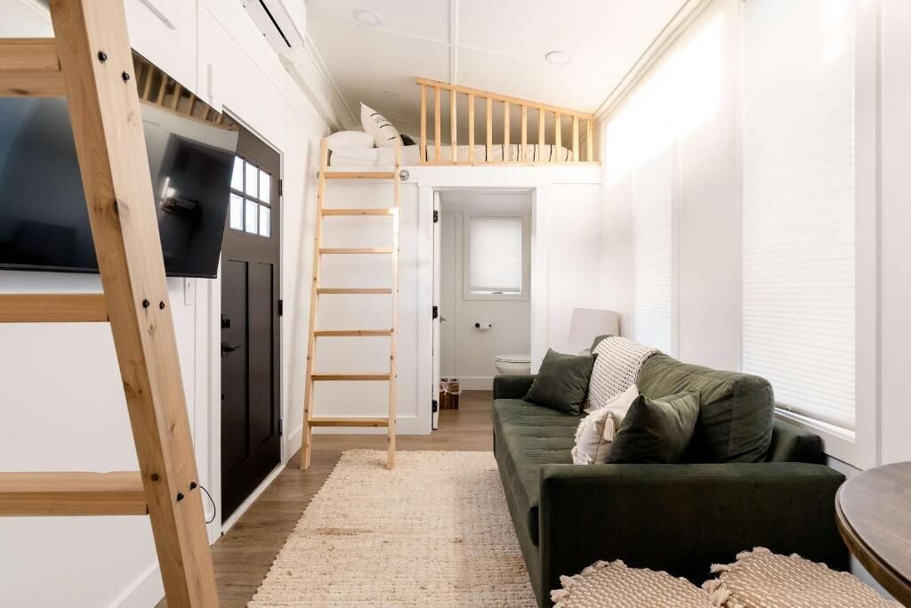 A compact living space with a bunk bed, a sofa, a small table, and a ladder.