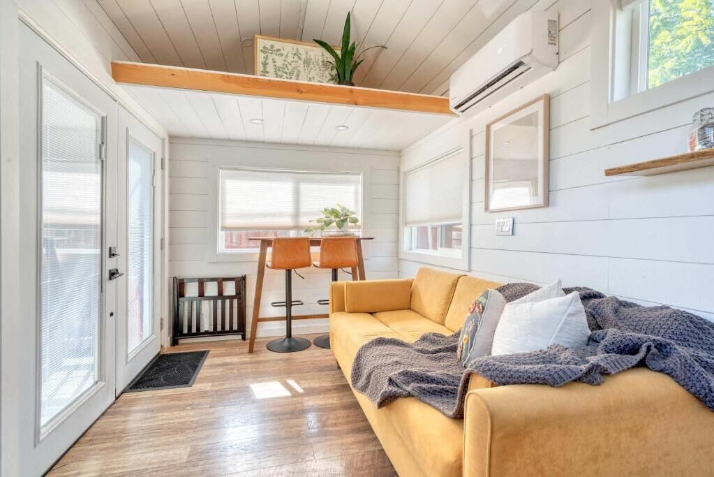 A compact living space with a sofa, a dining table with chairs, a radiator, and a large window.