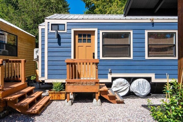 A blue mobile home with a wooden deck, a door, and windows.