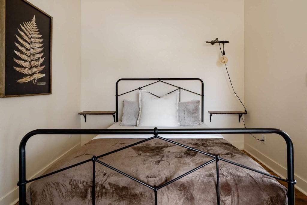 A bed with a metal frame, a headboard, two bedside tables, and a wall-mounted light fixture.