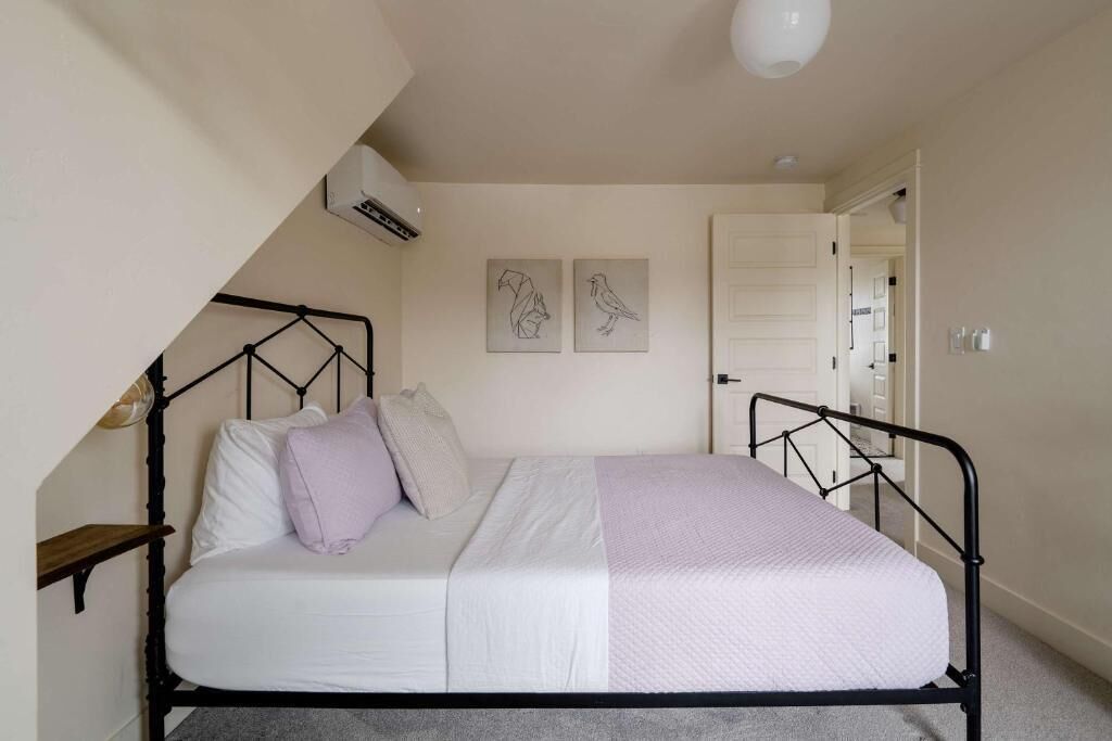 Een slaapkamer met een bed, een nachtkastje, een wandairconditioner en twee kunstwerken aan de muur.