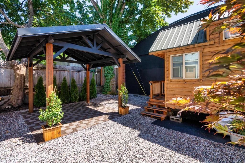 A wooden cabin with a covered patio, gravel ground, and potted plants.
