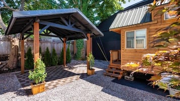 Eine Holzhütte mit überdachter Veranda, Kiesgrund und Topfpflanzen.