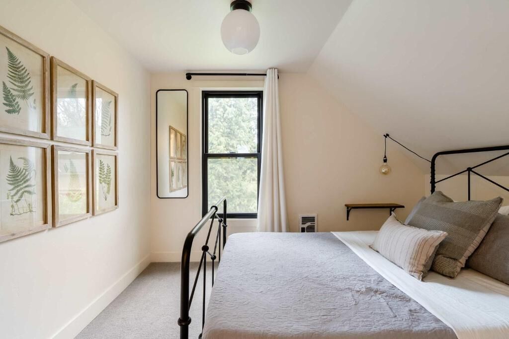 A bedroom with a bed, a window, and framed botanical prints on the wall.