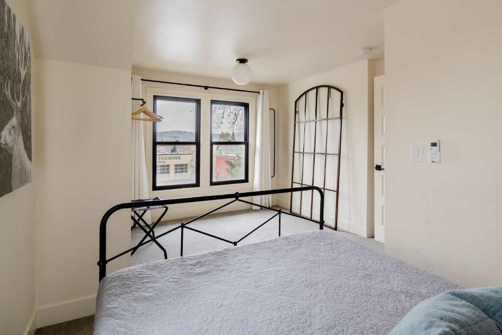 Une chambre à coucher avec un lit, une fenêtre donnant sur un paysage agréable, une porte et un luminaire fixé au mur.