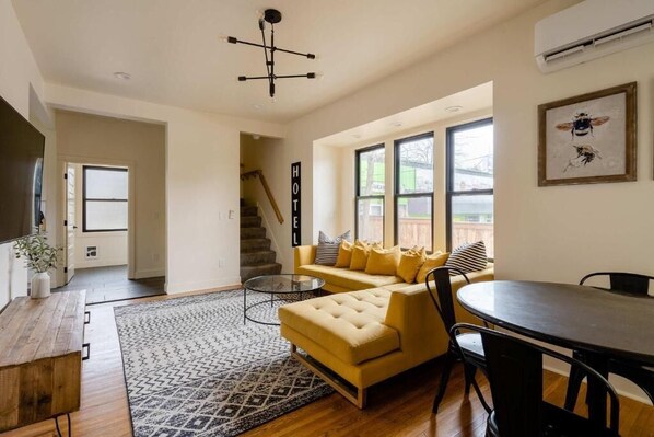 A modern living room with a sofa, a dining table, a coffee table, and a staircase leading to an upper level.