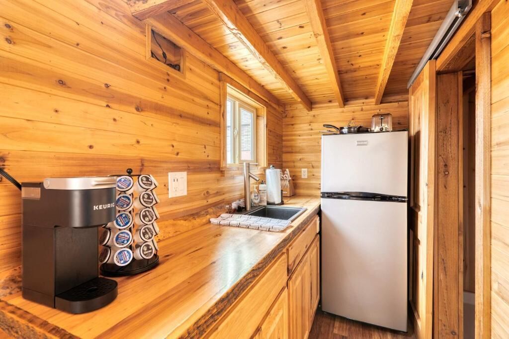Ein Holzblock-Interieur mit einer Küchenzeile, darunter eine Kaffeemaschine, ein Kühlschrank und ein Fenster.
