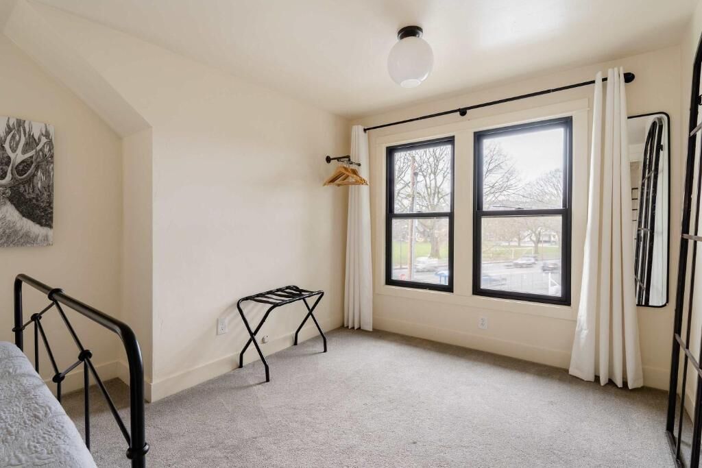 A room with a bed, a window with curtains, a radiator, and a coat rack.