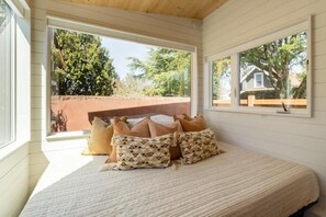 A bedroom with a bed, pillows, a window, and a view of the outside.