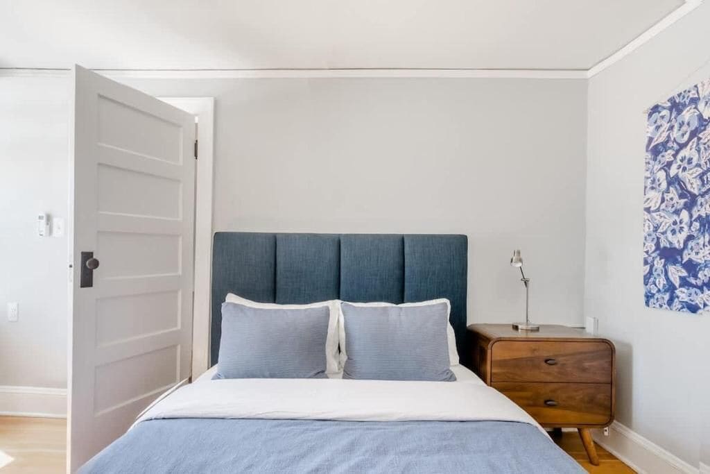 A bedroom with a bed, a nightstand, a door, and a wall with a floral pattern.