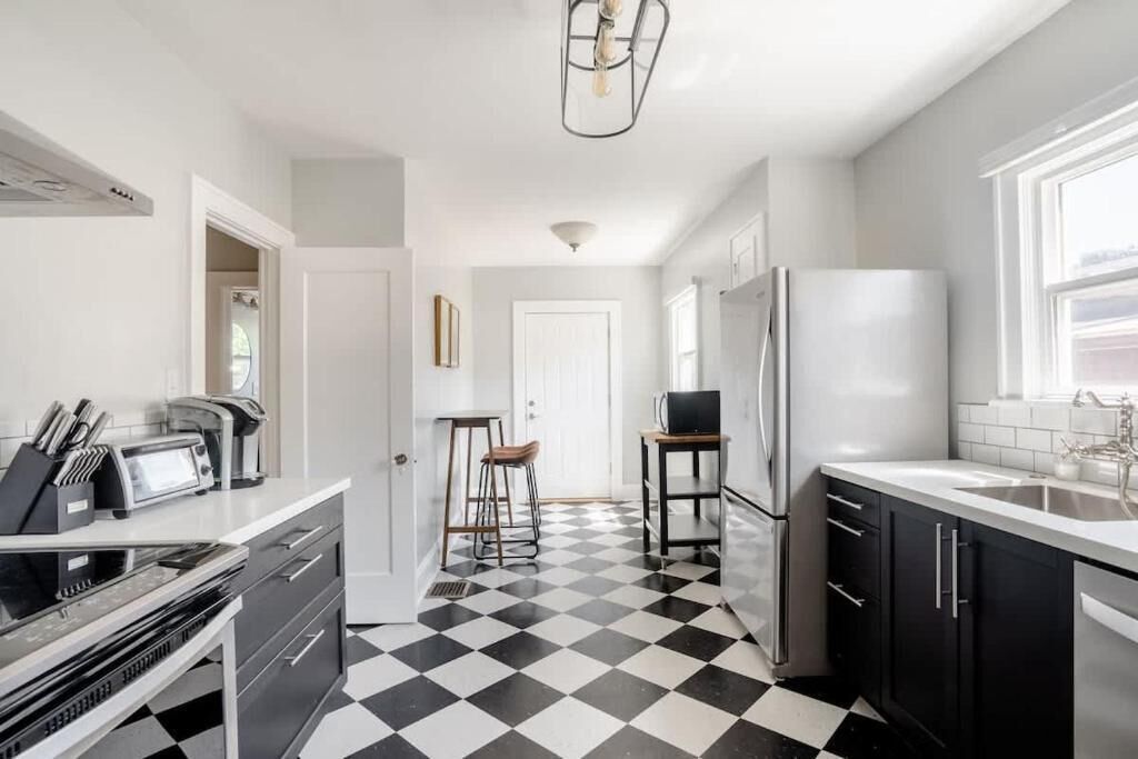 A kitchen with a black and white checkered floor, a refrigerator, a microwave, and a coffee machine.