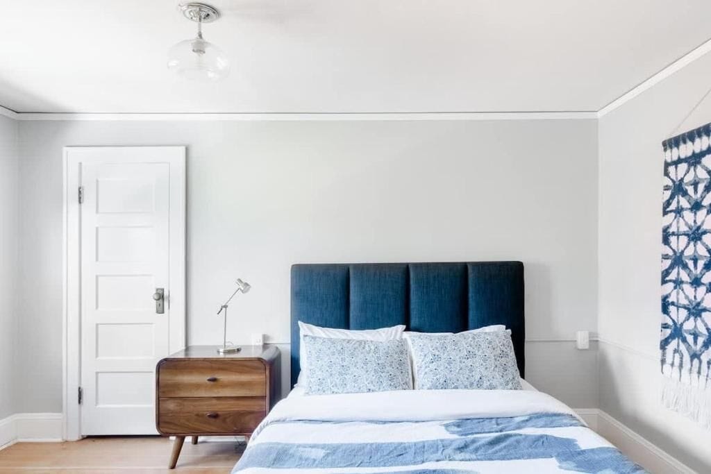 A bedroom with a bed, a dresser, a door, and a wall with a geometric pattern.