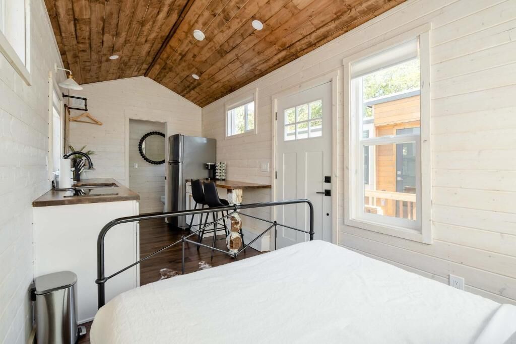 A room with a bed, a desk, a chair, a trash bin, and a window.
