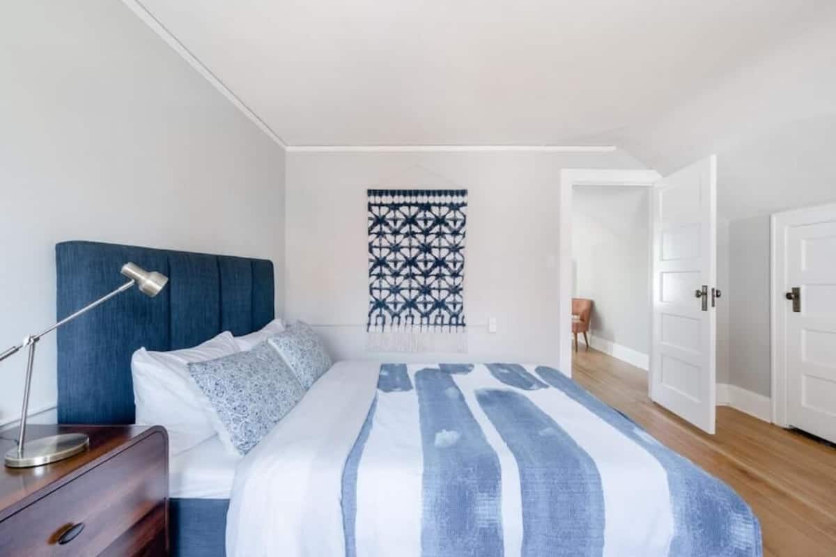 A bedroom with a bed, bedside table, lamp, and a wall hanging.