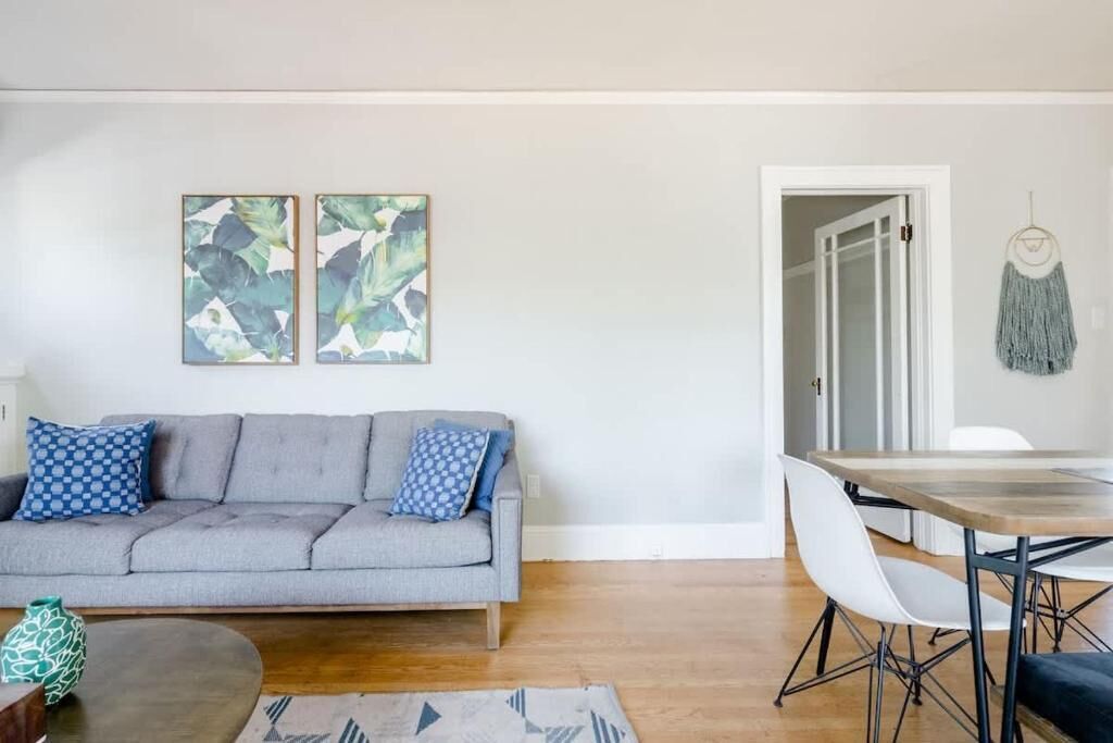 A living room with a grey sofa, a dining table with chairs, and two abstract paintings on the wall.