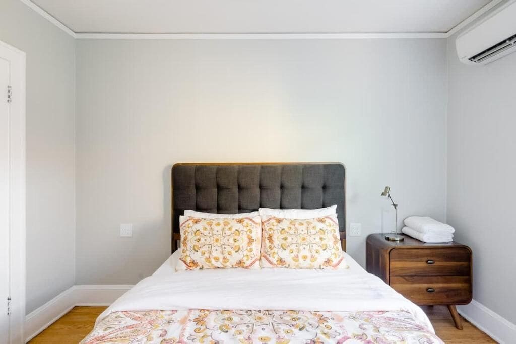 A bedroom with a bed, a nightstand, and a wall-mounted air conditioning unit.
