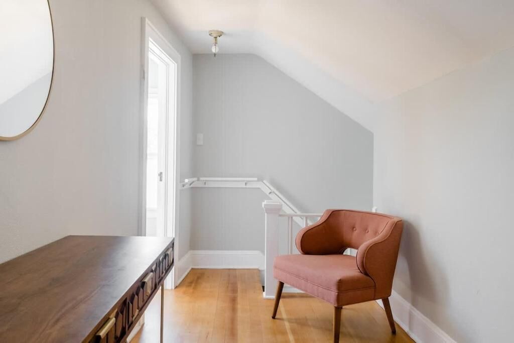 A room with a wooden floor, a pink chair, a white staircase, and a white door.