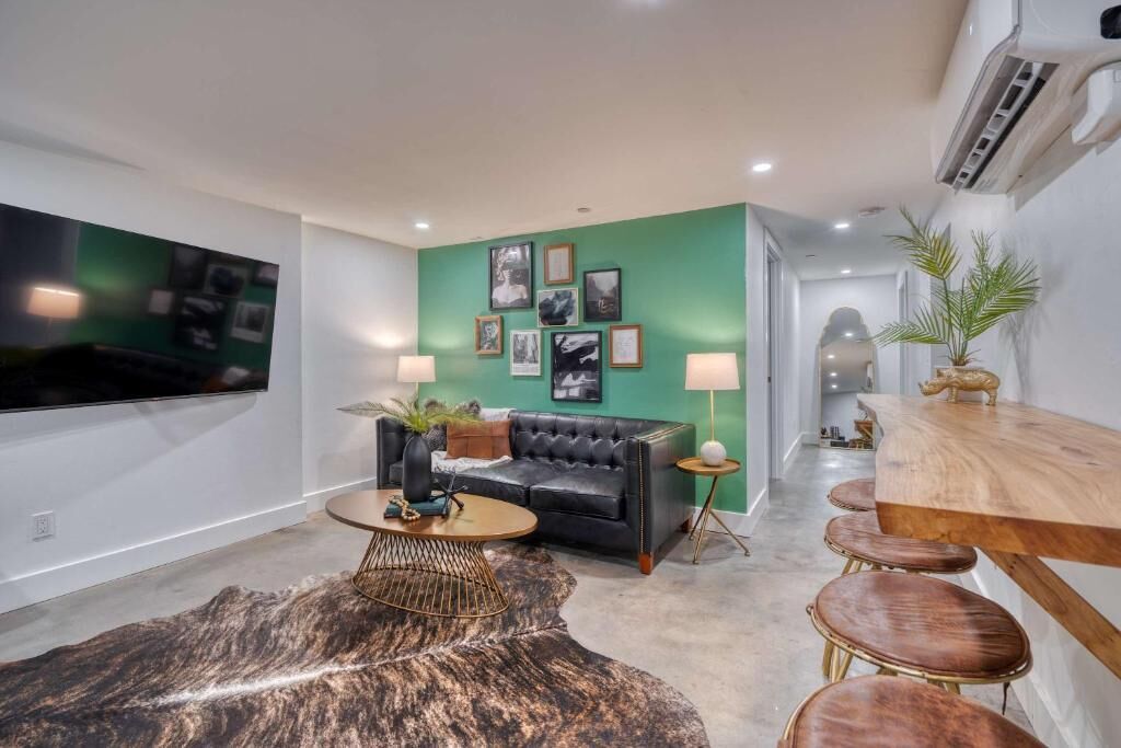 A modern living room with a black leather sofa, a round coffee table, and a green accent wall.