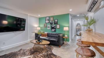 A modern living room with a black leather sofa, a round coffee table, and a green accent wall.