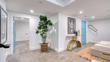 A modern interior with a concrete floor, a potted plant, a framed artwork, a blue door, and a bed.