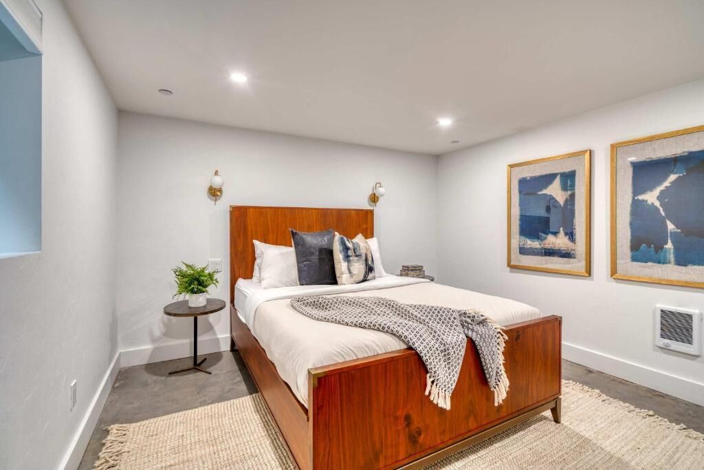 A bedroom with a wooden bed, a small round table with a plant, and two wall-mounted light fixtures.