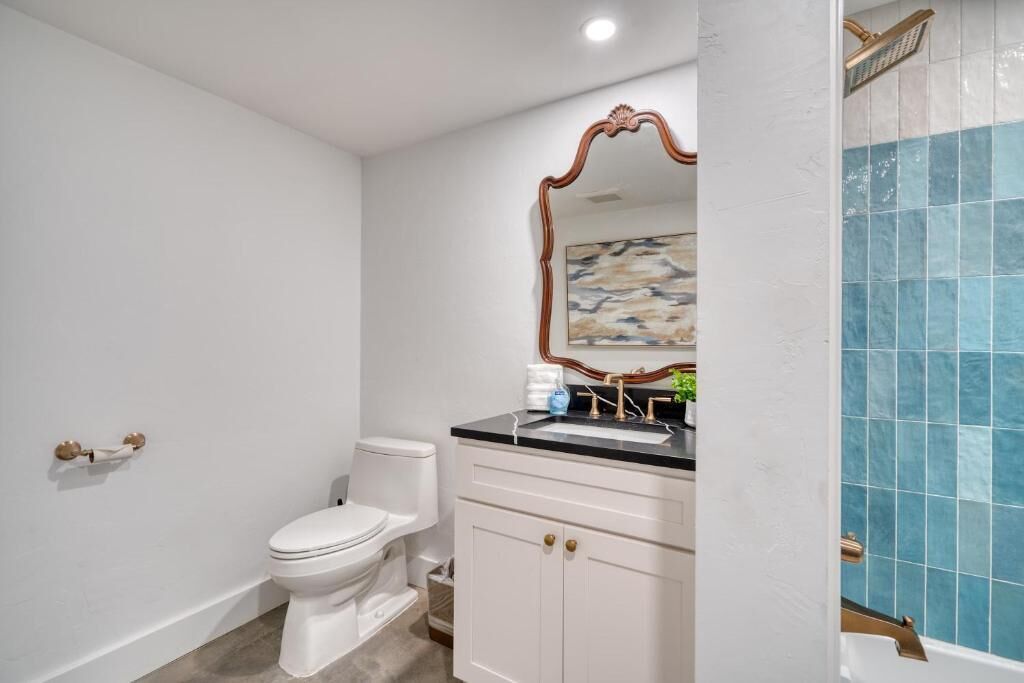 A bathroom with a white toilet, a vanity with a mirror, and a blue-tiled shower area.