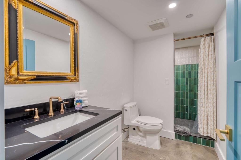 Un baño con lavamanos blanco, grifería dorada, inodoro blanco y cortina de ducha.