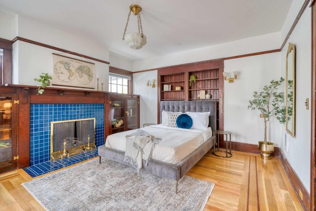 A bedroom with a bed, a fireplace, a bookshelf, and a mirror.
