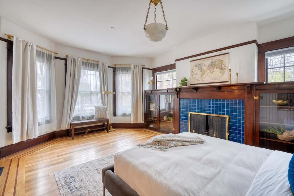 A bedroom with a large bed, a fireplace, a map on the wall, and a window with curtains.
