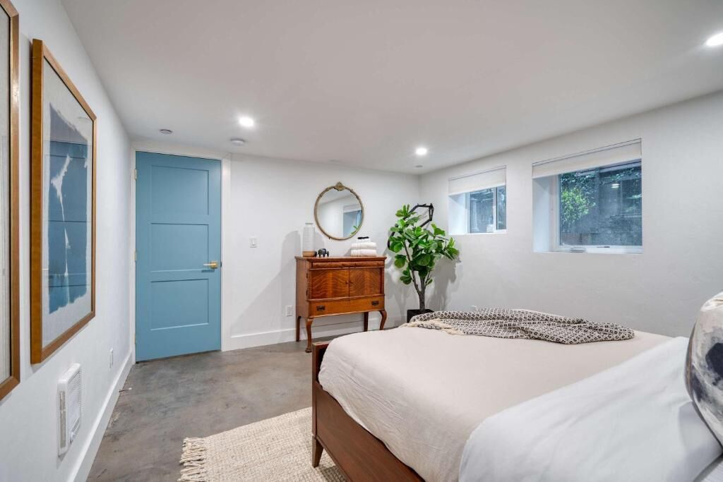 A bedroom with a bed, a dresser, a mirror, a plant, and a window.