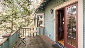 Um deck de madeira com um banco e uma mesa, uma porta com painéis de vidro e um corrimão de varanda.