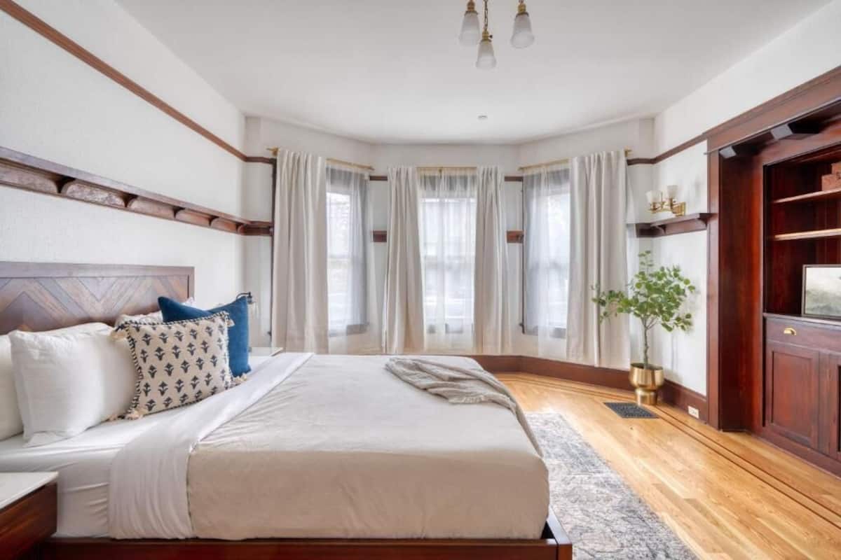 A bedroom with a large bed, wooden headboard, a nightstand, a bedside table, a potted plant, and a wooden wardrobe.