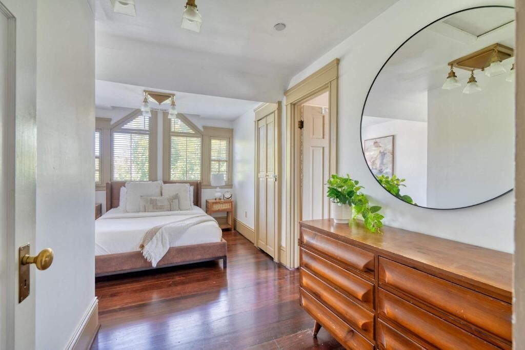 A bedroom with a bed, dresser, mirror, and a potted plant.