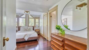 A bedroom with a bed, dresser, mirror, and a potted plant.