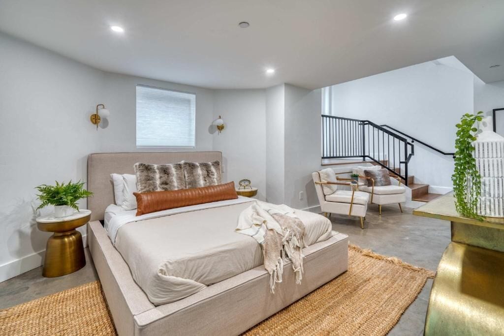 A modern bedroom with a large bed, a small seating area, a staircase, and a plant.
