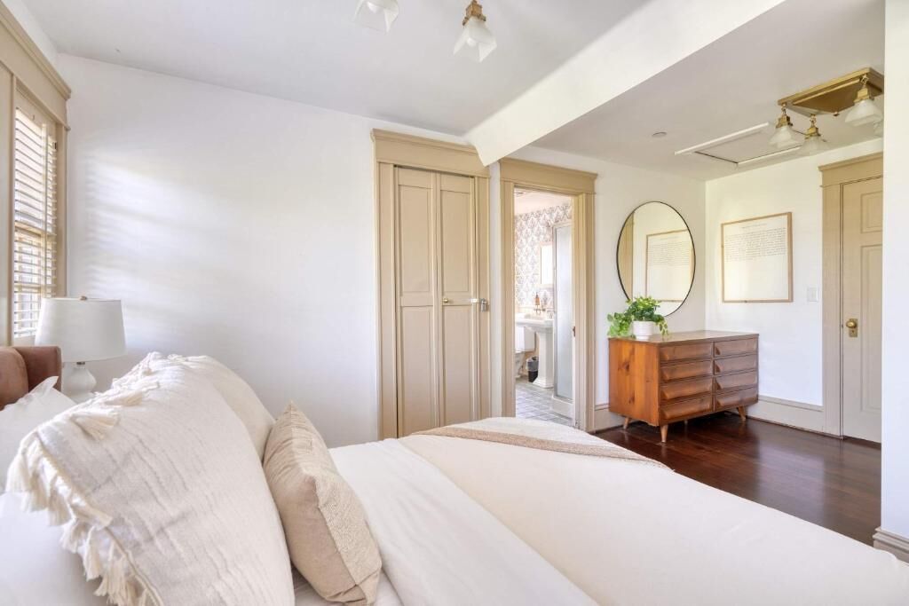 A bedroom with a bed, a dresser, a mirror, and a door leading to another room.