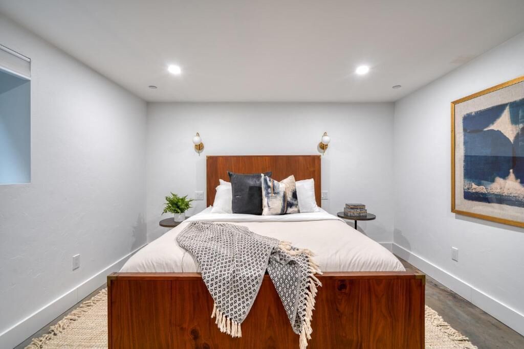 Ein modernes Schlafzimmer mit einem hölzernen Bett, weißer Bettwäsche und einem gerahmten Kunstwerk an der Wand.